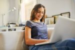 A girl lounges comfortably as she studies on her laptop.